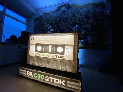 TDK SA-C90 cassette tape verlicht voor een poster met publiek erop