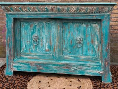 Blauwgroene geverfde kast met leeuwenkoppen, voor een muur, met een rieten mat ervoor op een tapijtje